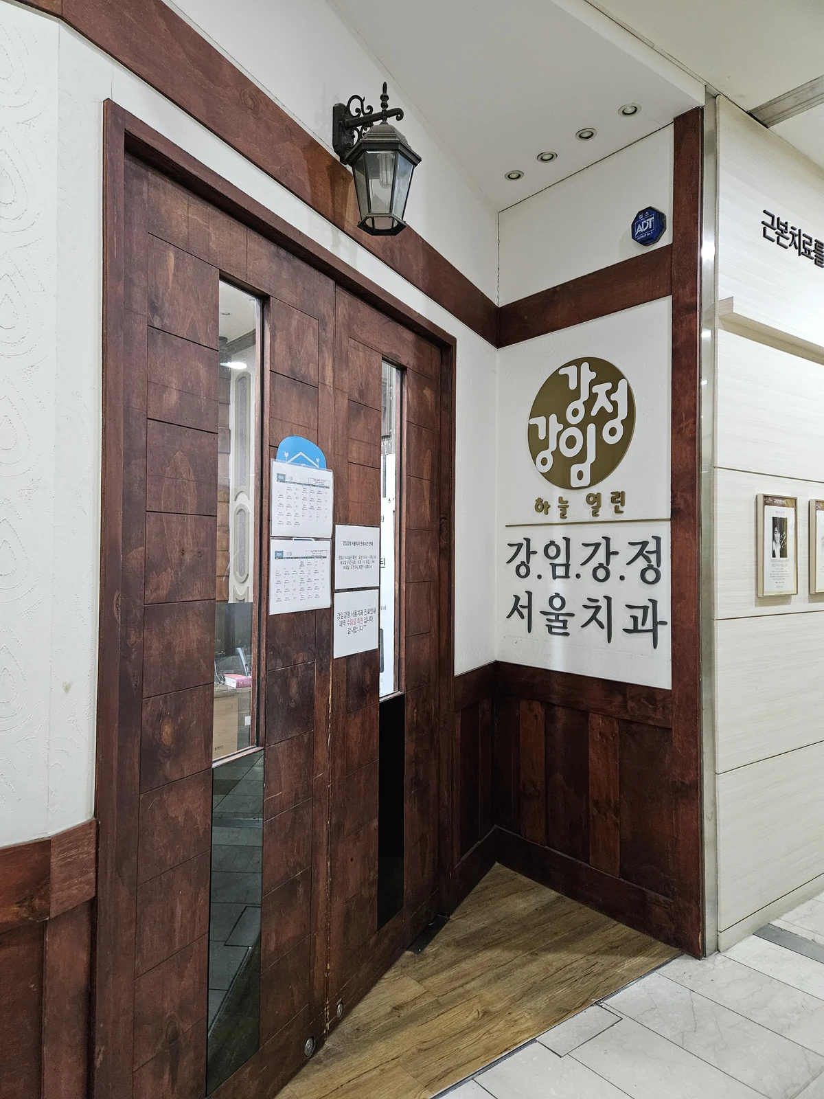 강임강정서울치과 간판과 나무 출입문 전체가 함께 보이는 병원 입구